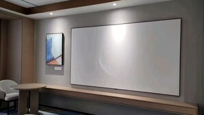 Una camera d'albergo moderna con una grande TV a parete, un tavolino rotondo e una sedia.