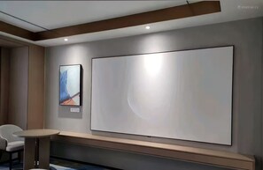 Una habitación de hotel moderna con un televisor grande montado en la pared, una mesita redonda y una silla.