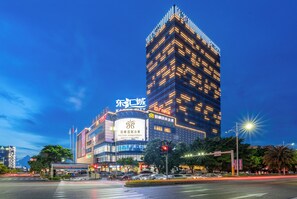Un hotel de varios pisos con un letrero llamativo que dice 'POLITTON INTERNATIONAL SERVICE APARTMENT' y un gran edificio iluminado al fondo.
