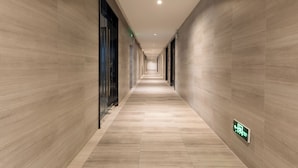 A long, narrow hallway with light-colored wooden walls and a tiled floor.