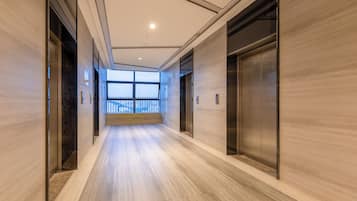 A corridor with wooden flooring, two elevators, and a large window at the end.