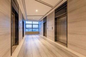 A corridor with wooden flooring, two elevators, and a large window at the end. -  Poltton International Apartments - Yangjiang Donghuicheng Plaza (Yangjiang)