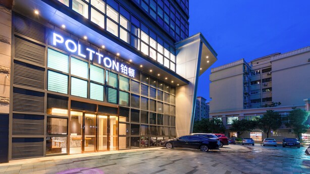 A hotel with a modern facade, large windows, and a parking lot with several cars.