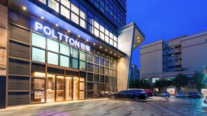 A hotel with a modern facade, large windows, and a parking lot with several cars.