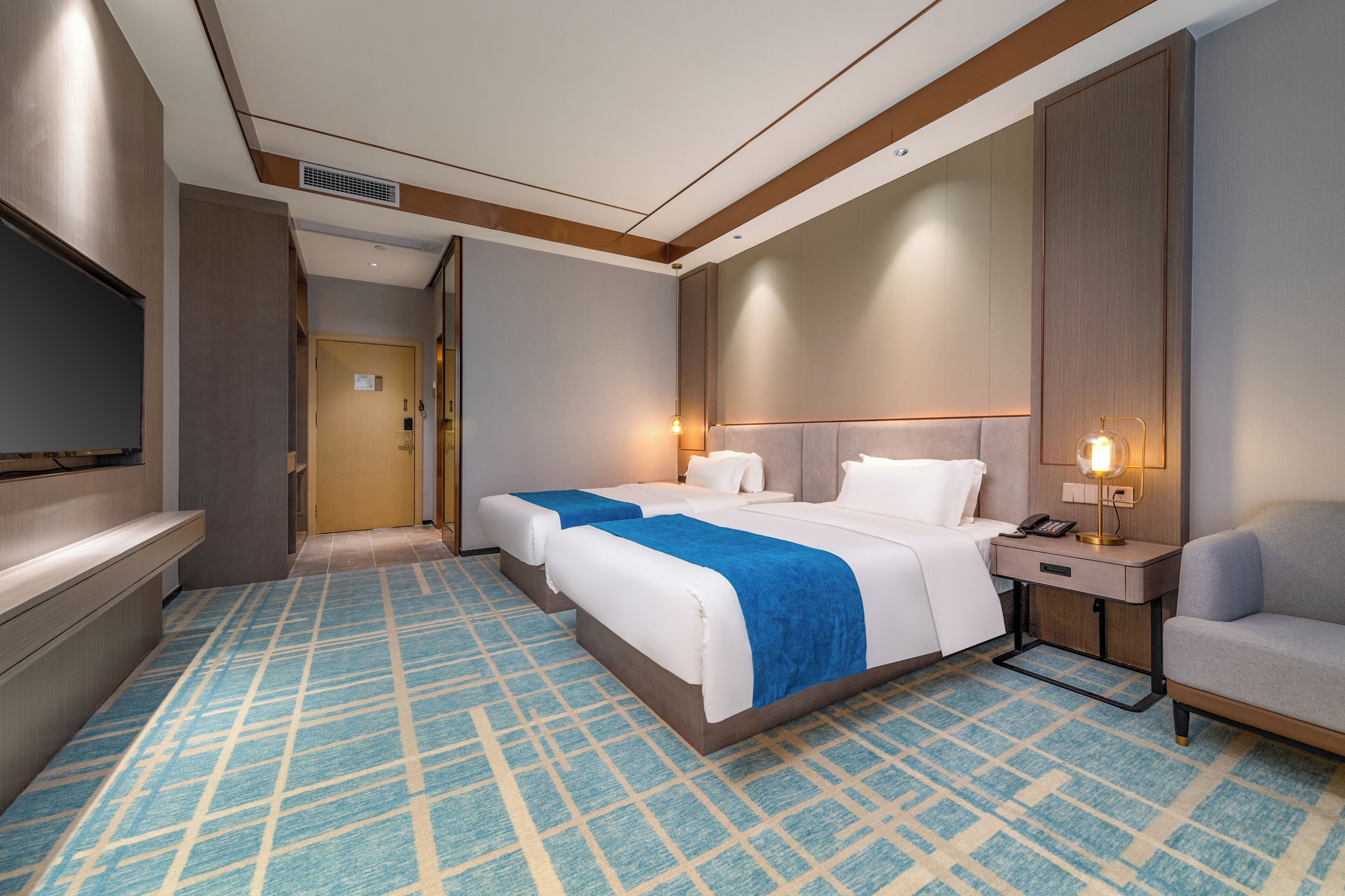 Ein Hotelzimmer mit einem großen Bett, Nachttischen, einem Fernseher und einem gemusterten Teppich.