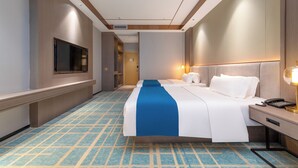 A hotel room with a large bed, bedside tables, a desk, a TV, and a patterned carpet.