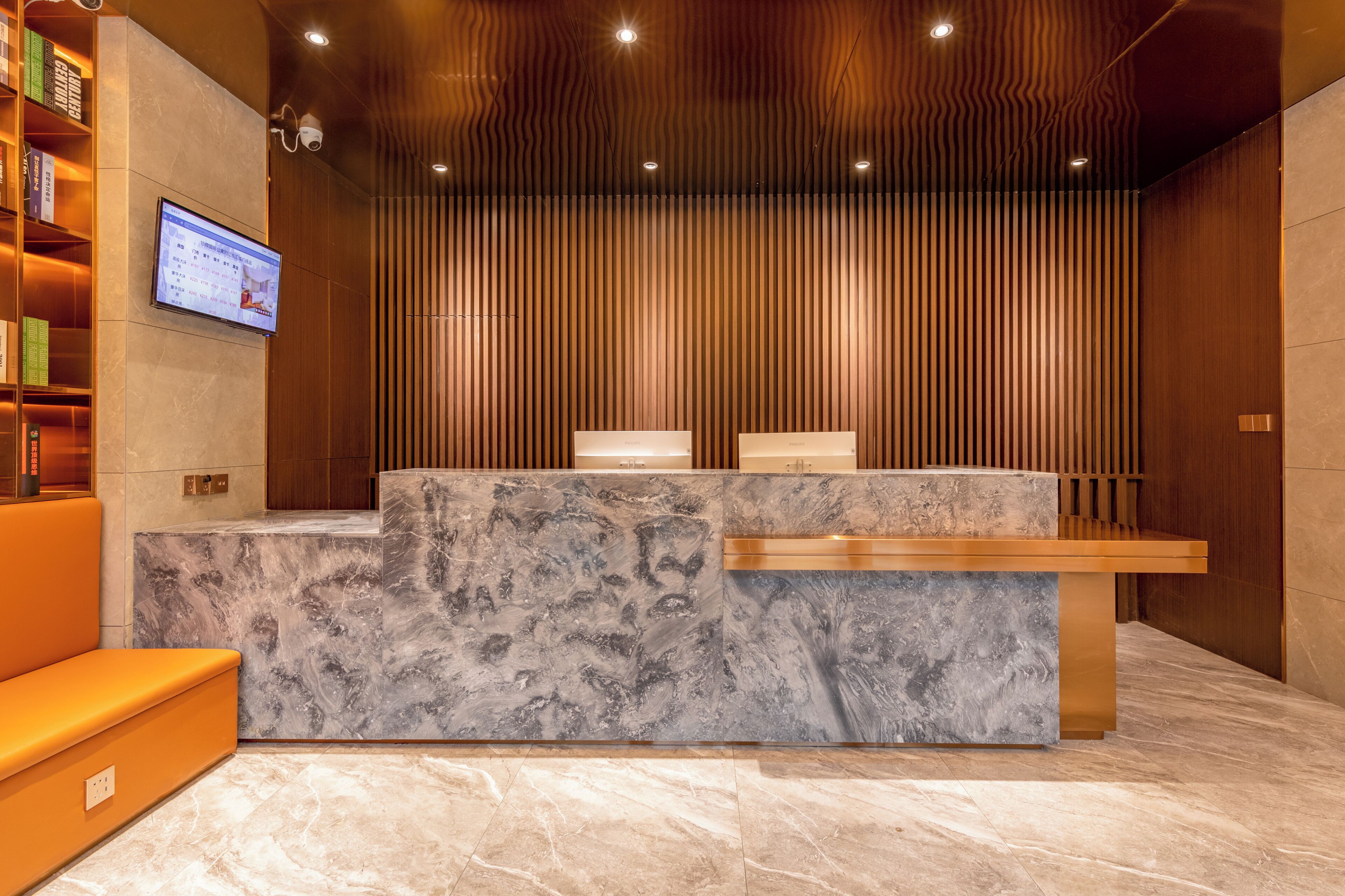 A reception desk with a marble top, a wooden panel wall, and a mounted television screen.