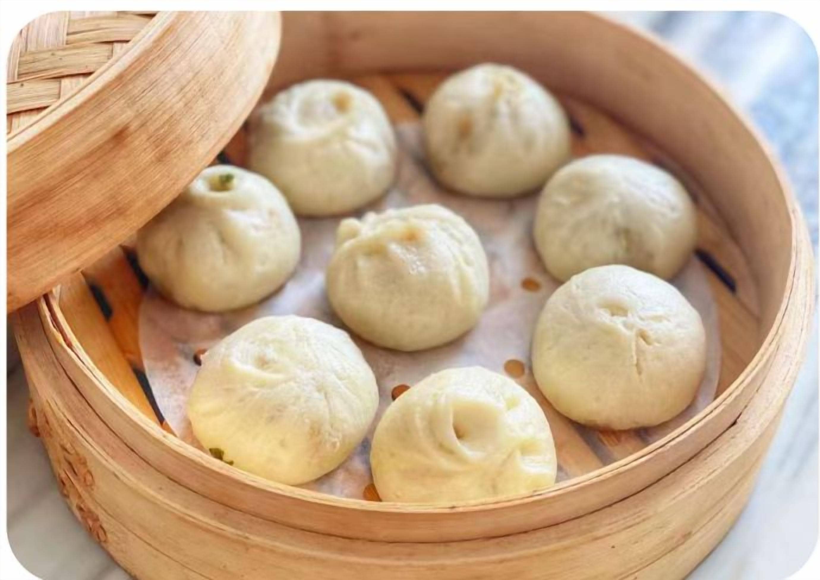 A bamboo steamer with several round, unfilled dough balls.