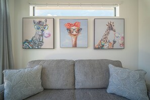 Ein Wohnzimmer mit grauem Sofa, gemusterten Zierkissen, einem Fenster mit Vorhängen und drei gerahmten Bildern an der Wand.