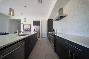 A modern kitchen with a large island, stainless steel appliances, and a tiled backsplash. - Reunion Haven Villa-1209 (Kissimmee)