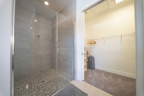 Ein modernes Badezimmer mit Duschkabine aus Glas, begehbarem Kleiderschrank und sichtbarem Stauraum.