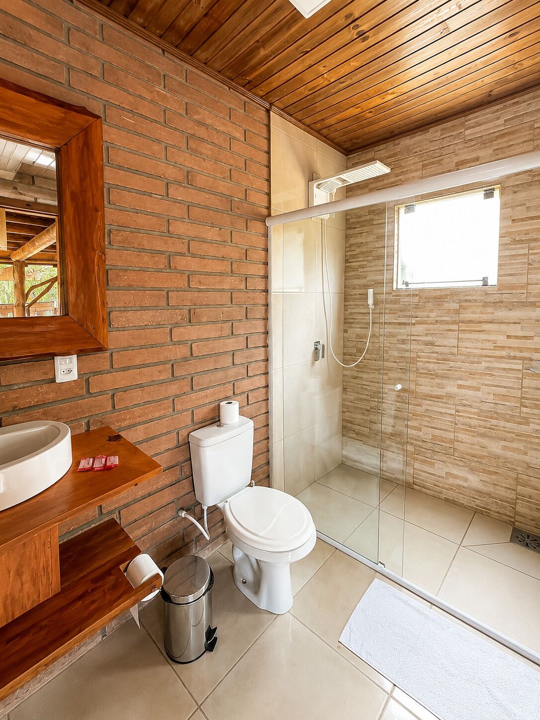 A modern bathroom with a wooden ceiling, a brick wall, a glass shower enclosure, and a white toilet.