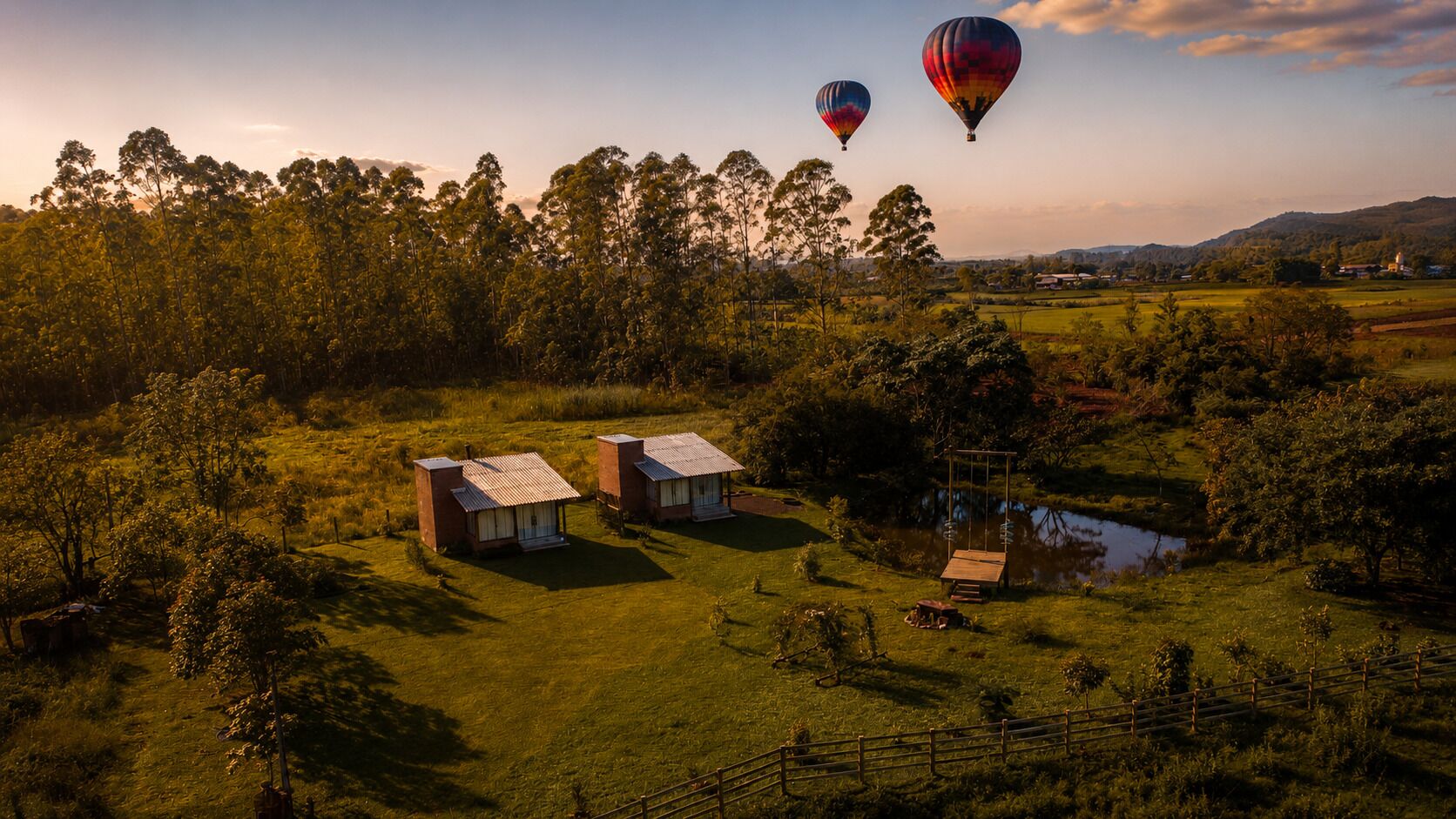 A rural landscape with two houses, a swing, and a hot air balloon in the distance.