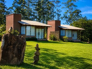 Una casa de dos plantas con fachada de ladrillo y techo de tejas, rodeada de un césped cuidado y árboles.
