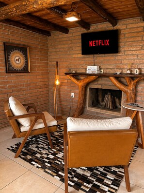 Una sala de estar acogedora con chimenea, un televisor montado mostrando 'NETFLIX' y una mesa de madera rústica.