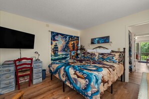A bedroom with a large bed, a desk, a chair, a television, and a painting on the wall. - Spacious Corolla retreat w/ hot tub and rec room! (Corolla)
