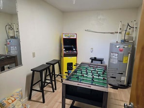A room with a foosball table, a Pac-Man arcade machine, and a water heater. - Spacious Corolla retreat w/ hot tub and rec room! (Corolla)