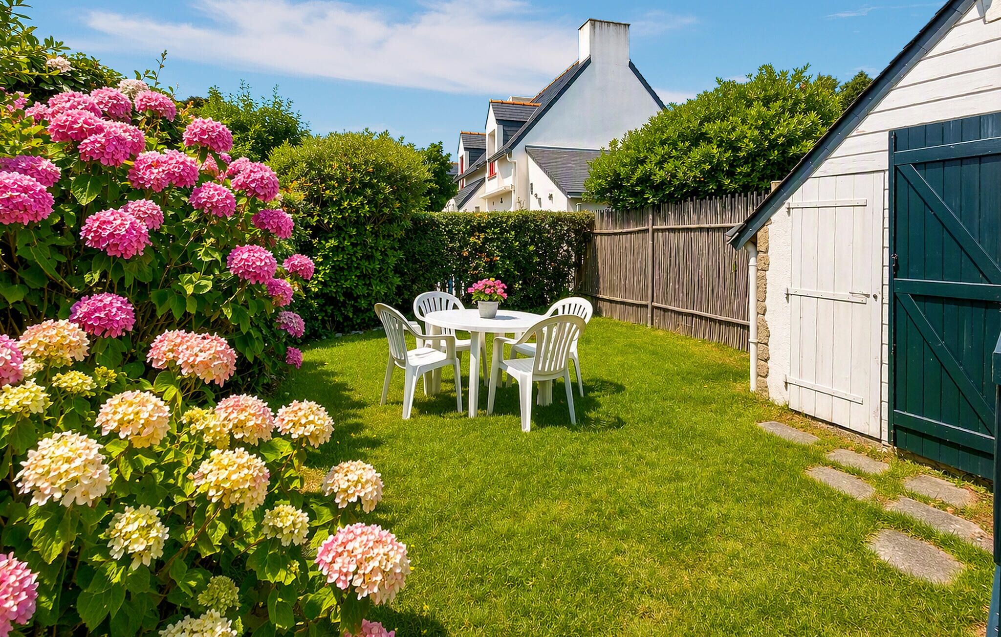 A well-maintained garden with a white table and chairs, surrounded by lush greenery and flowering plants.