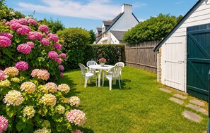 A well-maintained garden with a white table and chairs, surrounded by lush greenery and flowering plants. - 3 bedroom gorgeous home in Piriac-sur-Mer (Piriac-sur-Mer)
