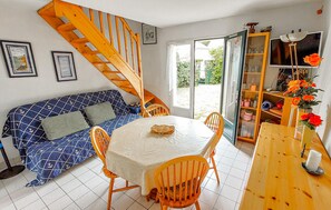 A room with a wooden staircase, a blue patterned sofa, a dining table with chairs, and a television on a wooden stand. - 3 bedroom gorgeous home in Piriac-sur-Mer (Piriac-sur-Mer)