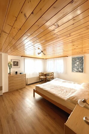 A bedroom with a wooden ceiling, a bed, a dresser, a chair, a table, and a radiator. - Moritzhaus, (Grächen), 1258 by Interhome (Grächen)