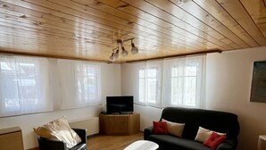 A cozy living room with a wooden ceiling, a black sofa, a white coffee table, and a television on a wooden cabinet. - Moritzhaus, (Grächen), 1258 by Interhome (Grächen)