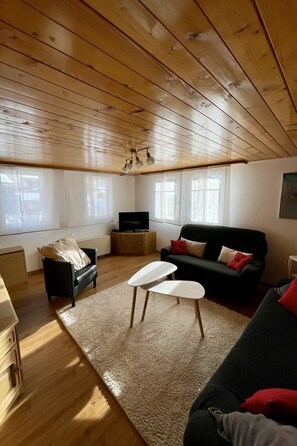 A cozy living room with a wooden ceiling, a black sofa, a white coffee table, and a television on a wooden cabinet. - Moritzhaus, (Grächen), 1258 by Interhome (Grächen)