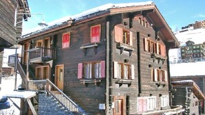 A multi-story wooden building with balconies and a staircase leading to the entrance. - Moritzhaus, (Grächen), 1258 by Interhome (Grächen)