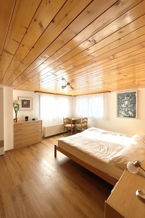 A bedroom with a wooden ceiling, a bed, a dresser, a desk with chairs, and a radiator. - Moritzhaus, (Grächen), 1258 by Interhome (Grächen)