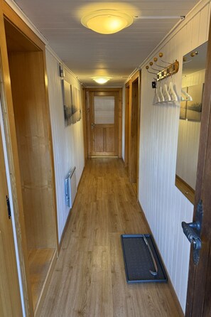 A narrow hallway with wooden flooring, a door with a metal handle, and a wall-mounted light fixture. - Moritzhaus, (Grächen), 1258 by Interhome (Grächen)