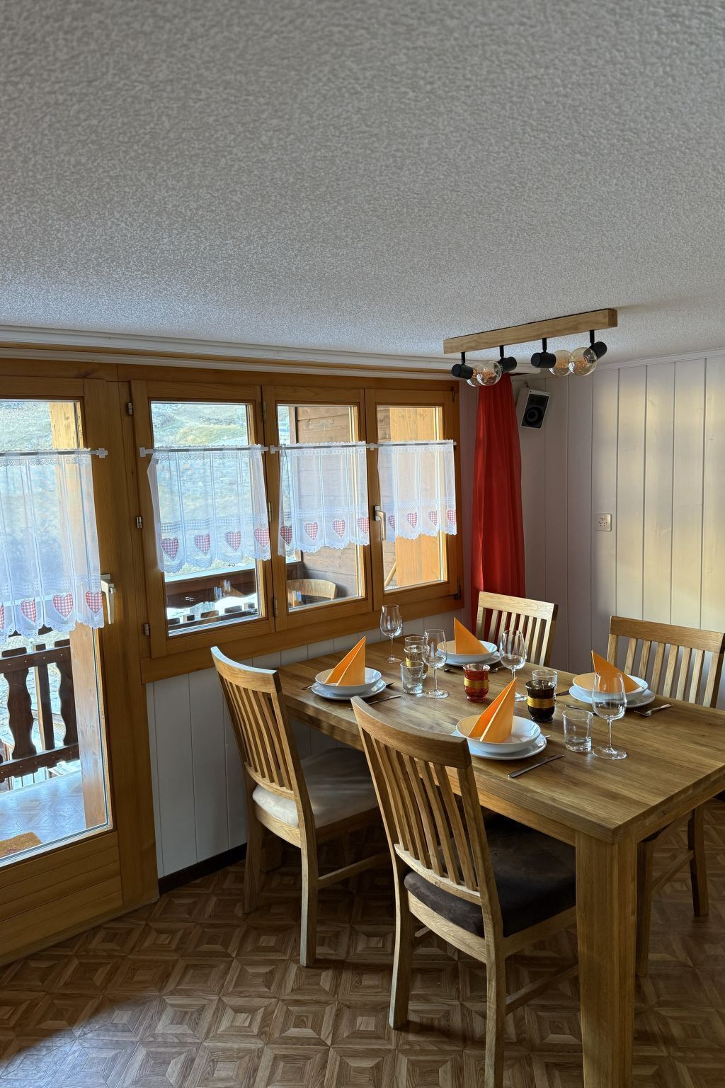 A dining area with a wooden table set for four, surrounded by chairs.