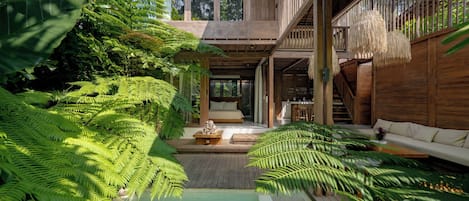 A modern, multi-level wooden structure with a central courtyard, a bed, seating area, and a small pool.