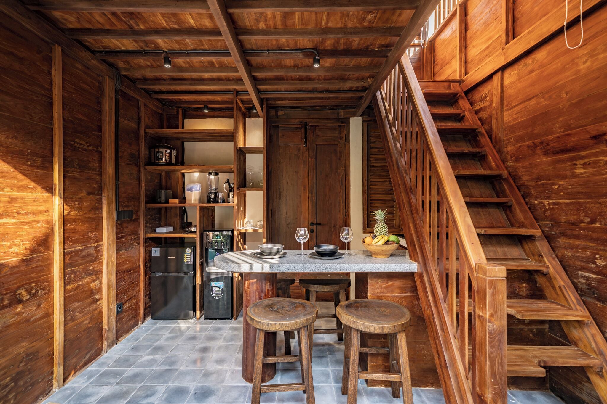 Un interior de madera con cocina, una mesa de comedor y taburetes, y una escalera.