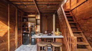 A wooden interior with a kitchen area, a dining table with stools, and a staircase. - Haven by The River Ubud (Ubud)