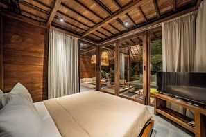 Un dormitorio con una cama grande, un televisor sobre un mueble de madera y vistas a un jardín a través de puertas de cristal.