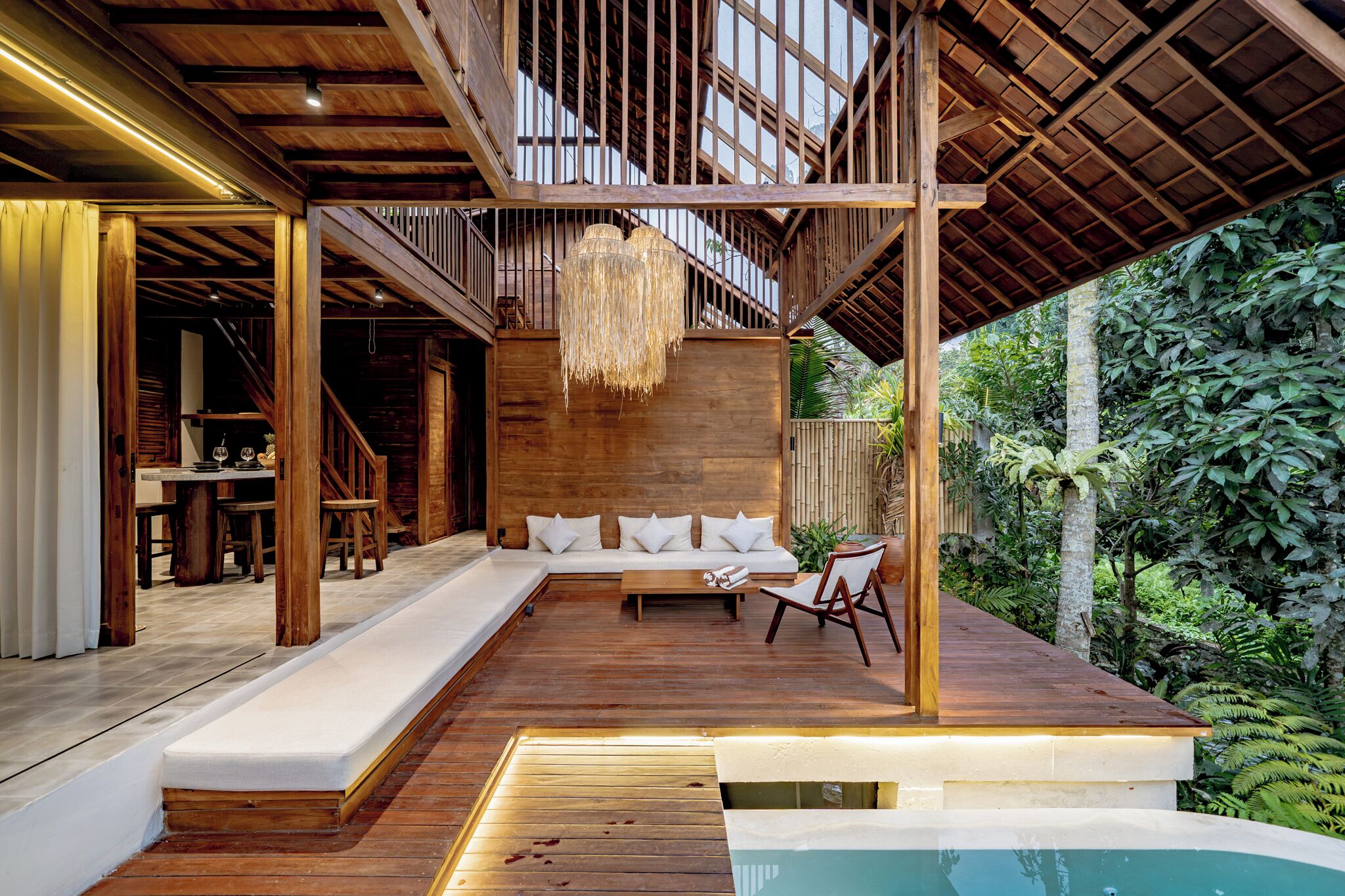 Una terraza de madera con un sofá, una zona de comedor y una piscina.