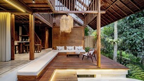 A wooden deck with a sofa, a dining area, and a pool. - Haven by The River Ubud (Ubud)