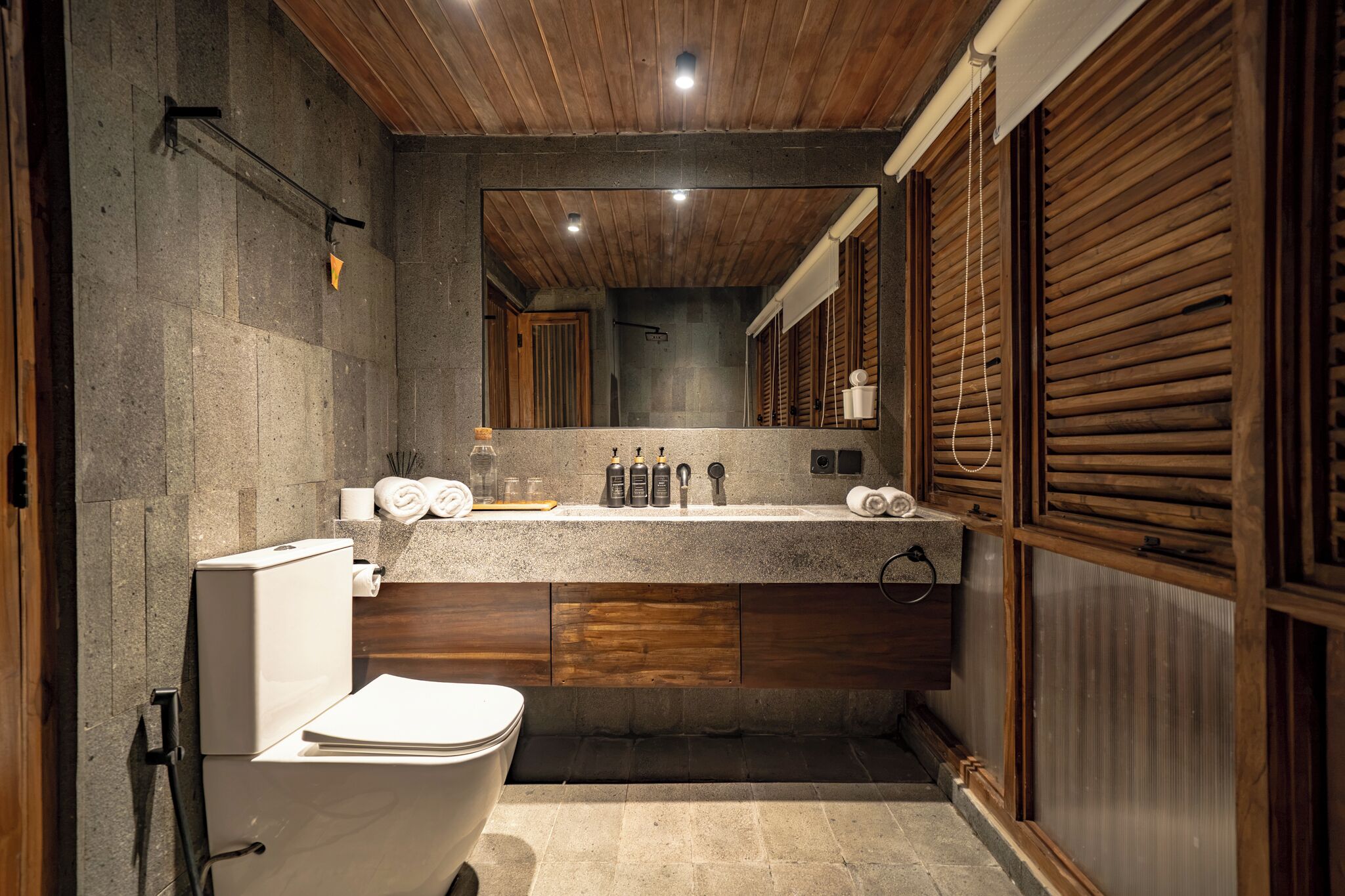 Un baño con inodoro, lavamanos y artículos de aseo, y paneles de madera.