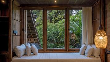 Habitación de madera con un banco empotrado, una escalera y vistas de abundante vegetación.