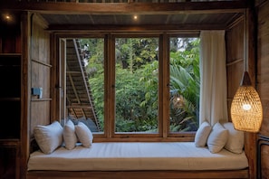 Habitación de madera con un banco empotrado, una escalera y vistas de abundante vegetación.