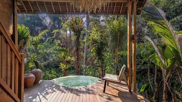 Una terraza de madera con un jacuzzi, rodeada de exuberante vegetación tropical.