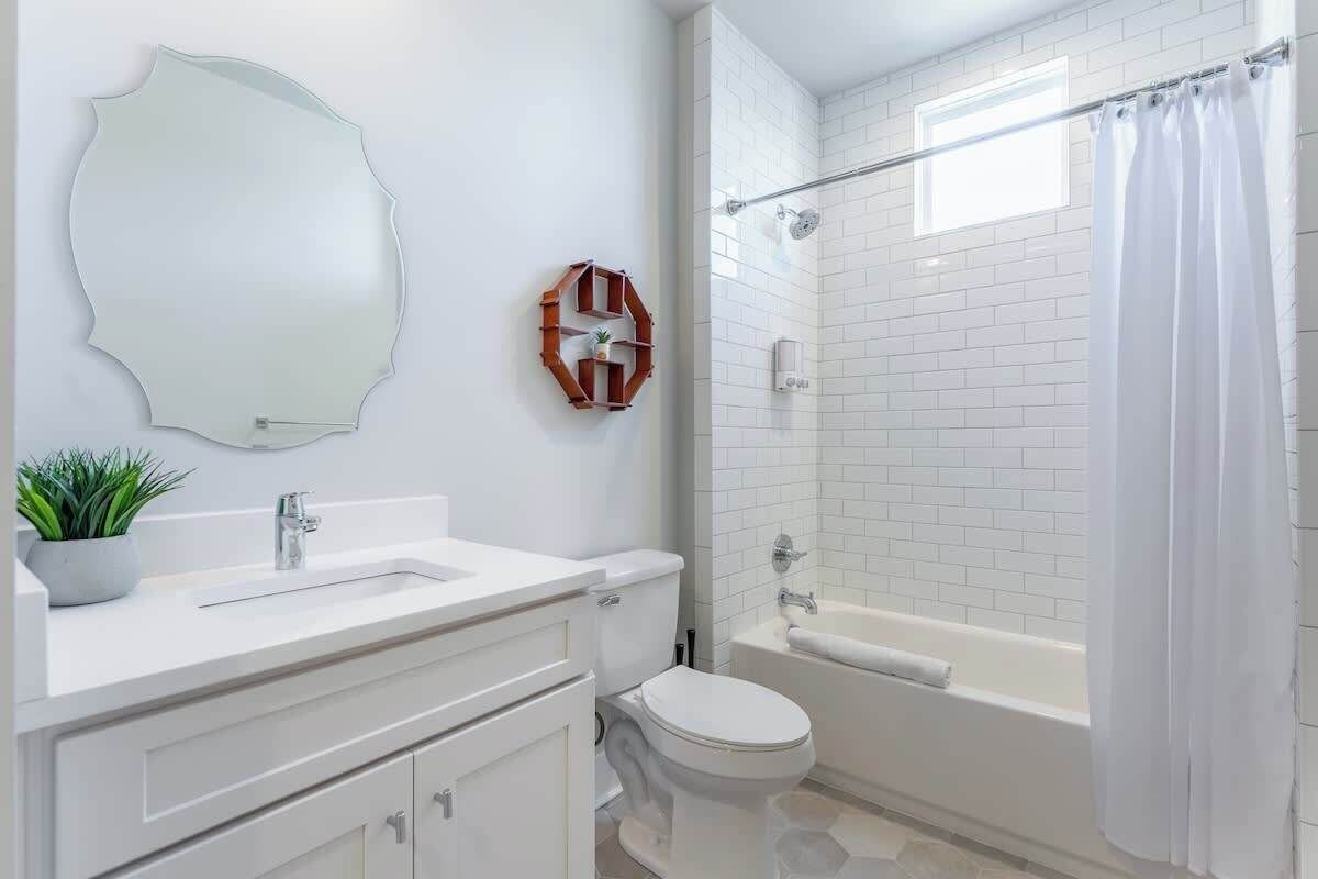A bathroom with a white sink, toilet, and bathtub. There is a shower curtain, a mirror, and a potted plant on the counter.
