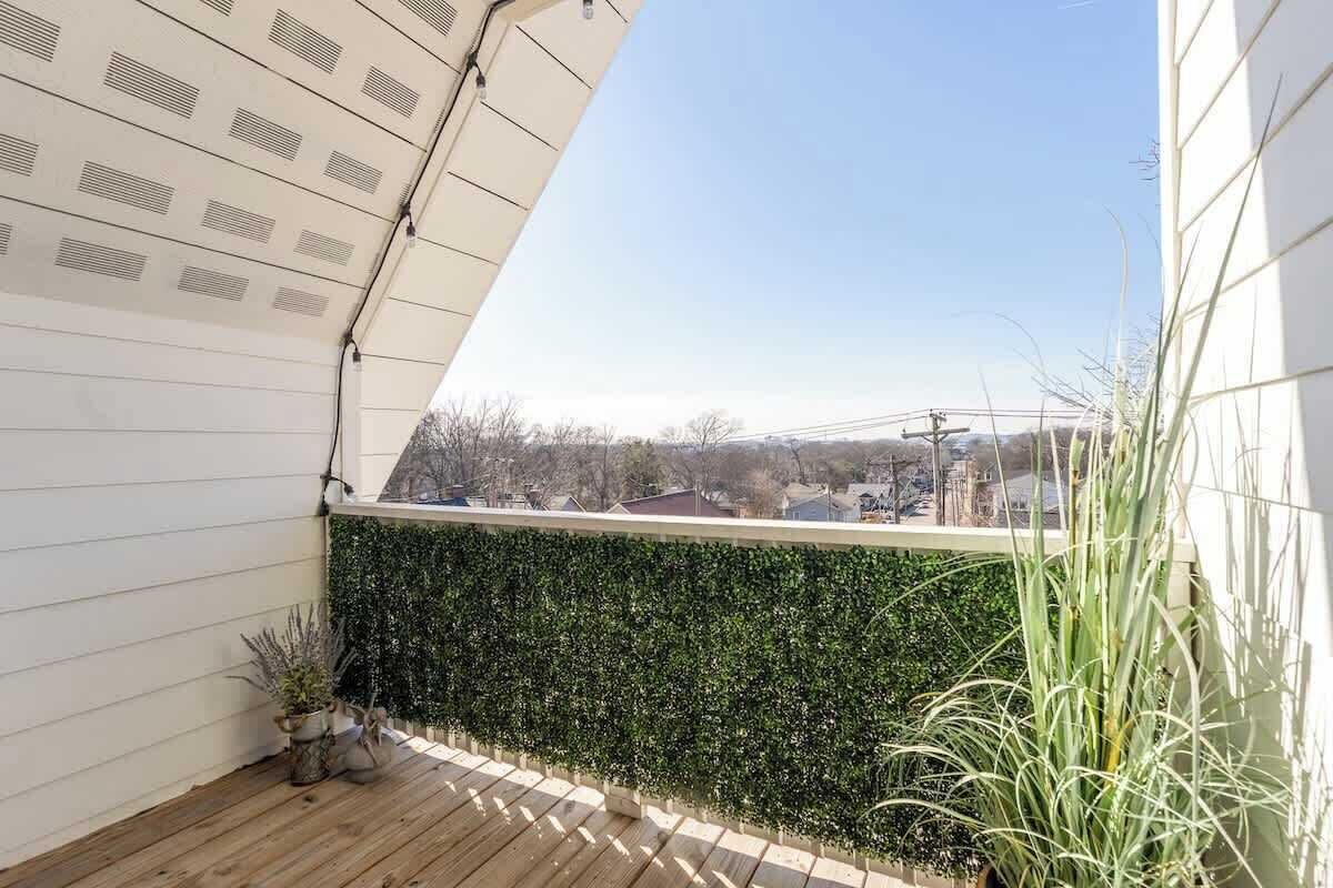 Ein Balkon mit Blick auf eine Stadtlandschaft, einem grünen Heckenstreifen und einem Holzboden.
