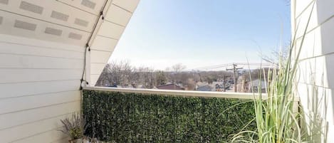Un balcon donnant sur un paysage urbain, une haie verdoyante et un plancher en bois.