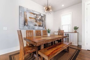 A dining area with a wooden table, chairs, a bench, a pendant light, and a large abstract painting on the wall. - 4BR East Nashville - Walk to Bars & Restaurants (Nashville)