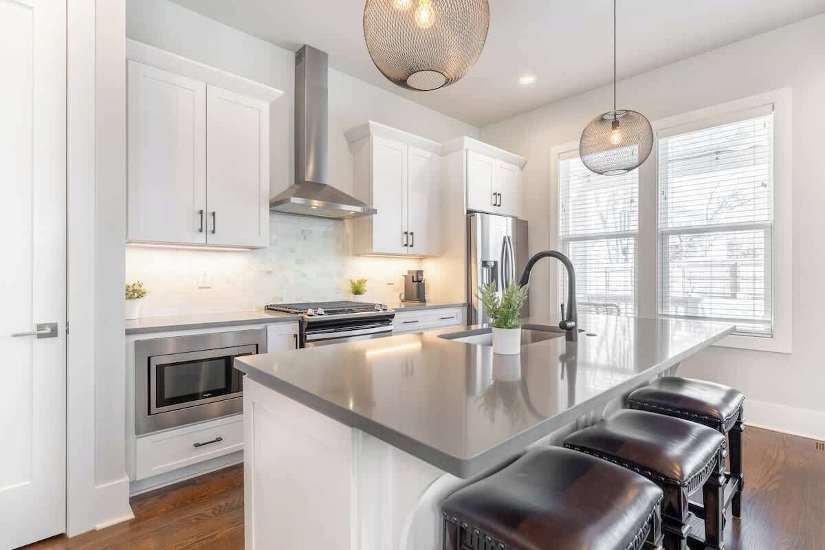 A modern kitchen with white cabinetry, stainless steel appliances, and a central island with bar stools.