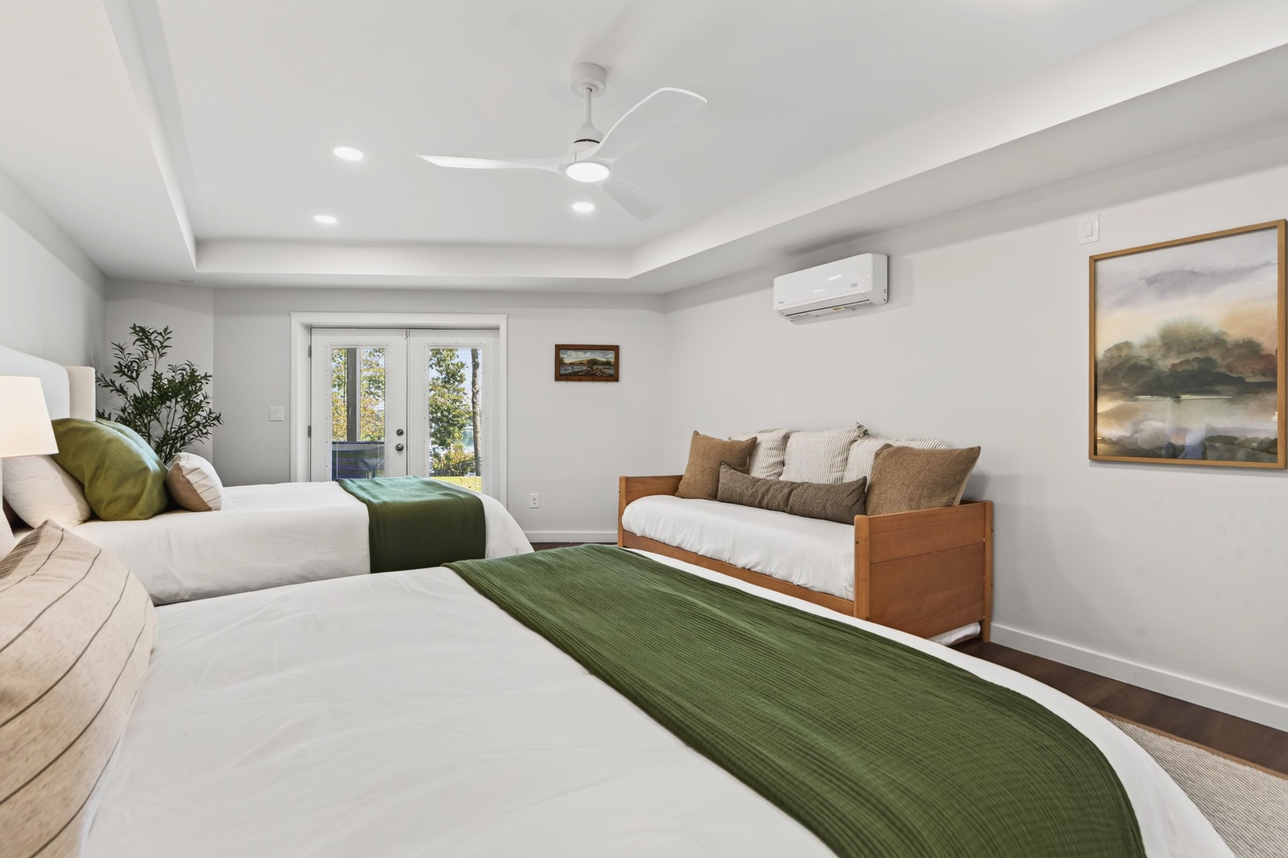 Ein Hotelzimmer mit zwei Betten, einem Deckenventilator, einer Klimaanlage, einem Fenster mit Blick und einem Bild an der Wand.