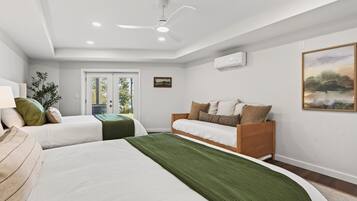 Ein Hotelzimmer mit zwei Betten, einem Deckenventilator, einer Klimaanlage, einem Fenster mit Blick und einem Bild an der Wand.