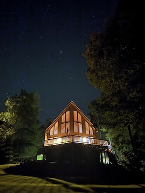 Eine zweistöckige Holzhütte mit Balkon, umgeben von Bäumen, in der Nacht.