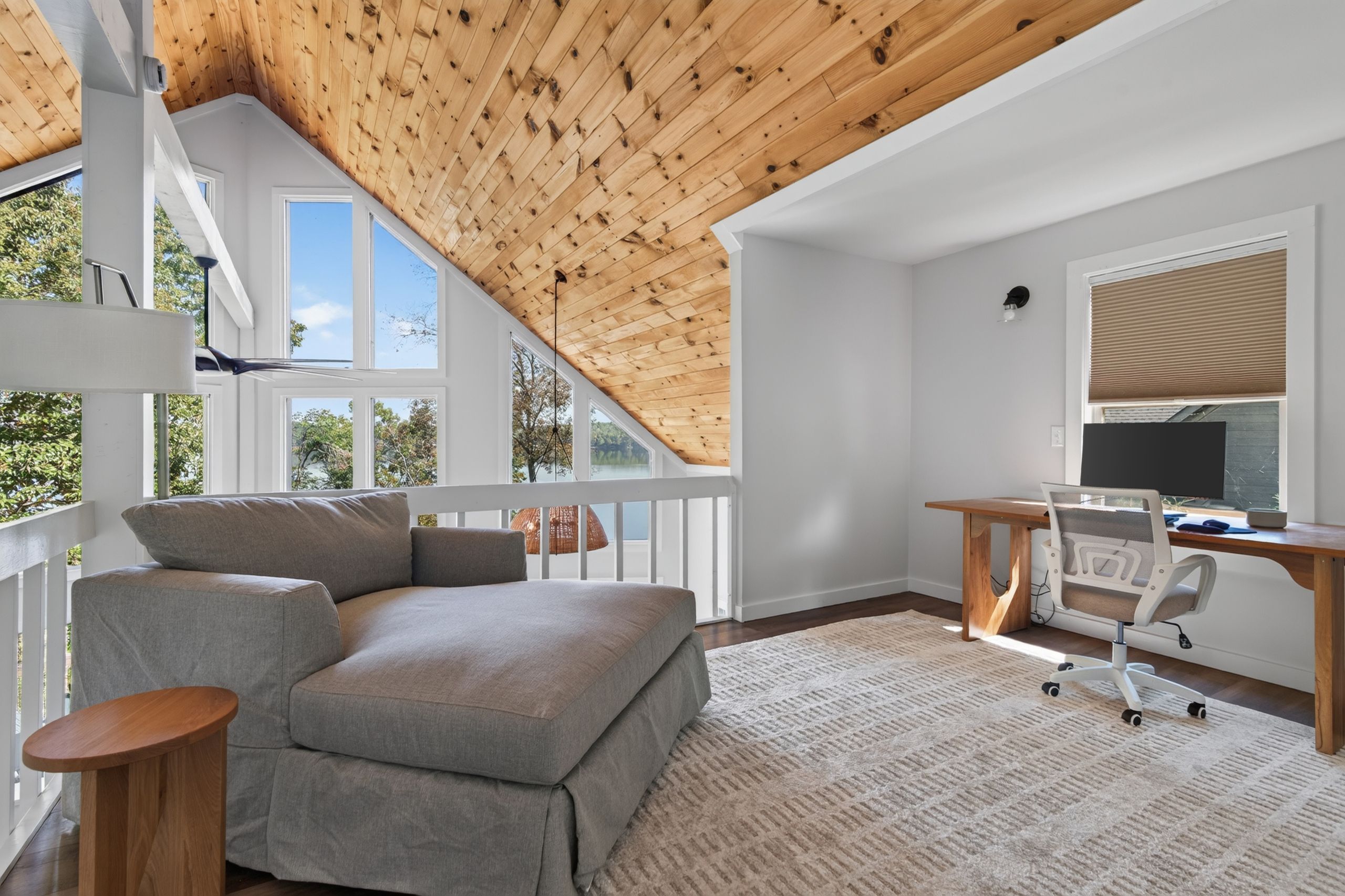Ein modernes Schlafzimmer im Loftsstil mit schrägverdeckter Decke, einem grauen Sofa, einem Holztisch und einem großen Fenster.